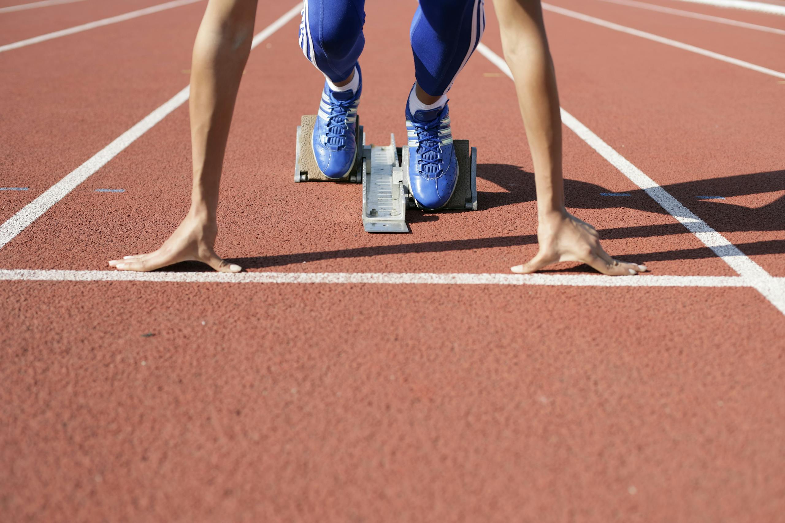 Close-up of an athlete starting a race at the track field on a sunny day.
